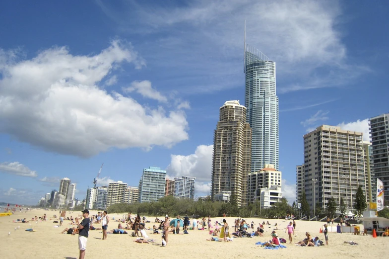 many people are relaxing on a sandy beach with tall buildings