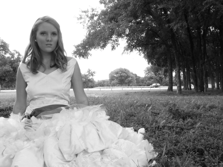 the girl in the white gown sits on the grass