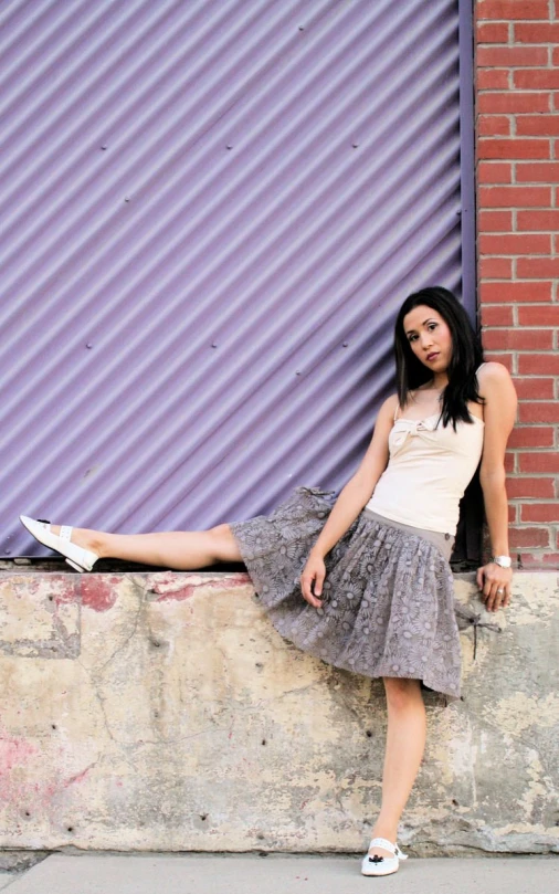 a young woman leans against a concrete wall