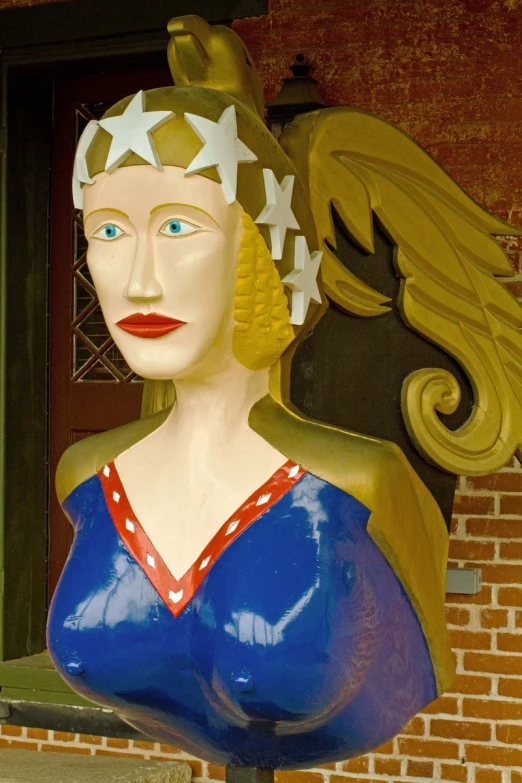 a statue of a woman in a blue dress stands by a brick wall