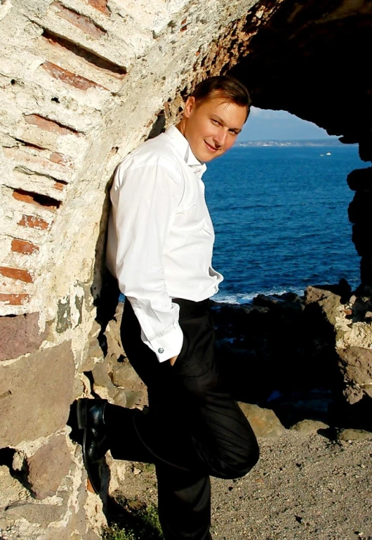 a man wearing a white shirt and black pants standing next to a rocky wall