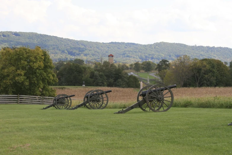 three large guns sitting in a field with some hills behind them