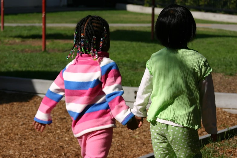 two children holding hands walking on grass