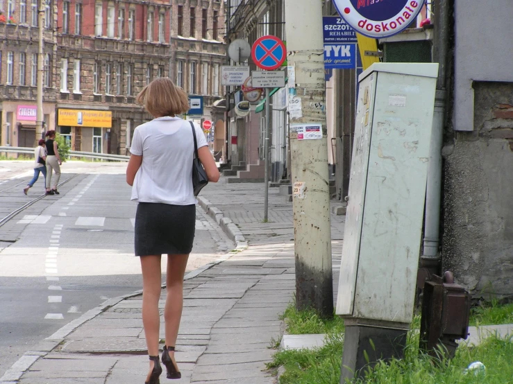 the woman is walking down the sidewalk beside the street sign