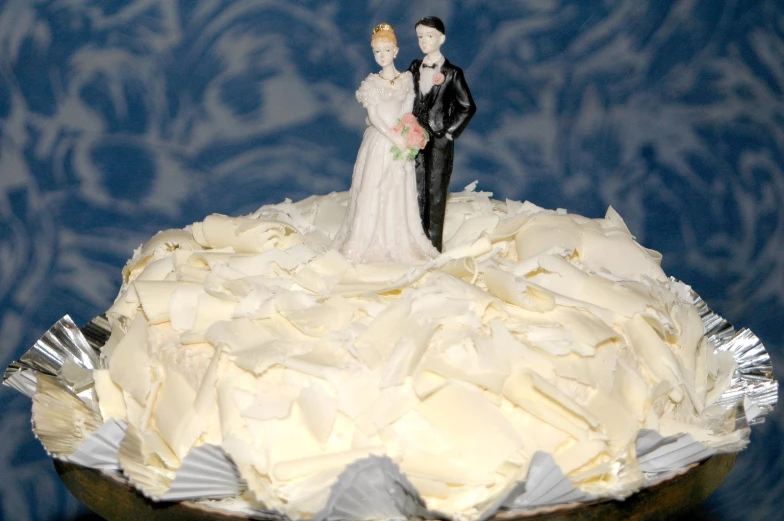 a bride and groom figurine stand next to each other, atop a wedding cake