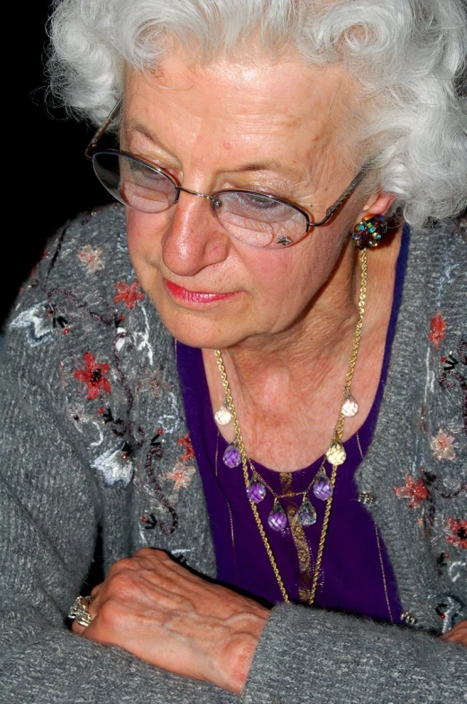 an elderly woman sitting down at a table with a pen and eyeglasses