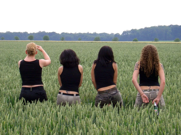 four girls stand in a green field, looking out into the distance