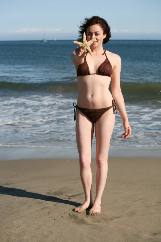 a woman in a brown bikini holds a starfish