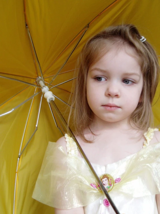 a little girl in a white dress holding a yellow umbrella