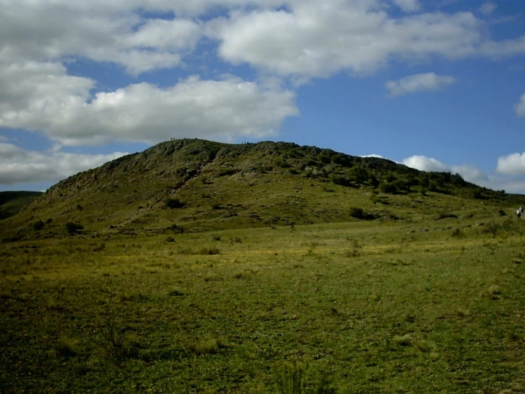 people walking across the grass towards the top of a hill