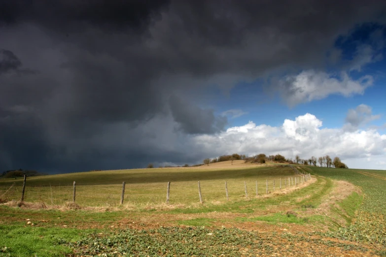 a field with a fence under stormy skies