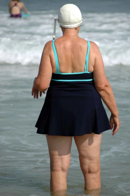 the back of a woman in a skirt and hat standing in the ocean