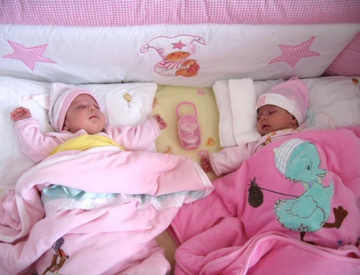 two baby girls laying in bed with blankets