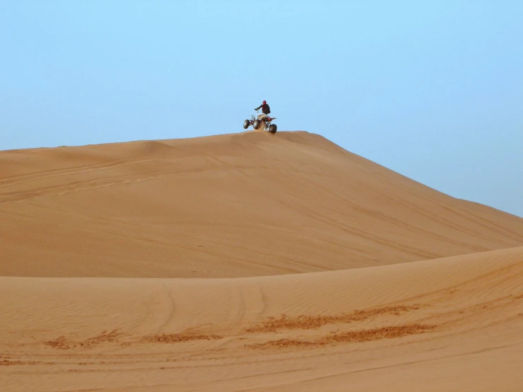 two people riding motorcycles on top of a large, sandy hill