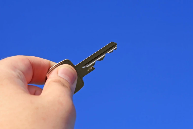 a hand holding a small key in the middle of a clear blue sky