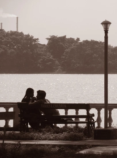 a couple is sitting on a bench looking at a lake