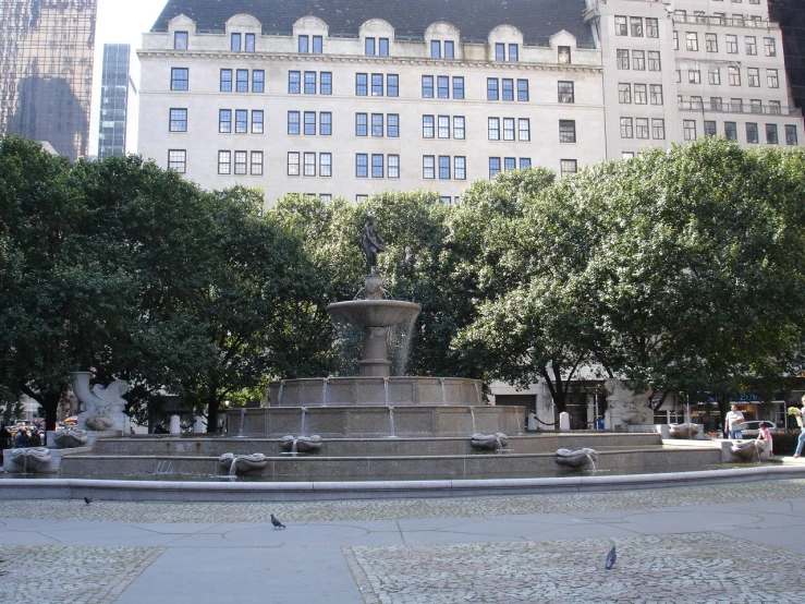 the fountain in the middle of a plaza with people walking around