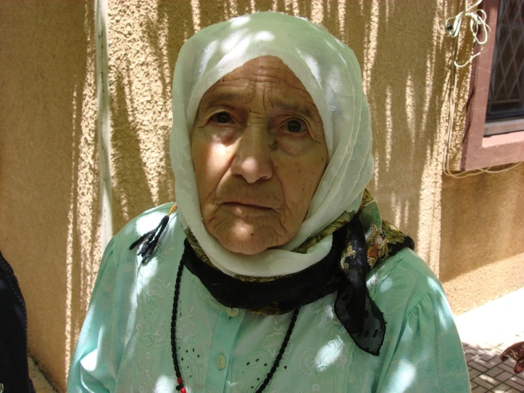 an elderly woman wearing a green jacket and headdress looking concerned