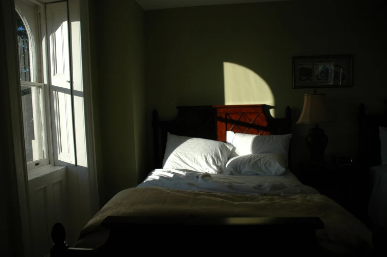 a bed sitting under two window sills next to a light