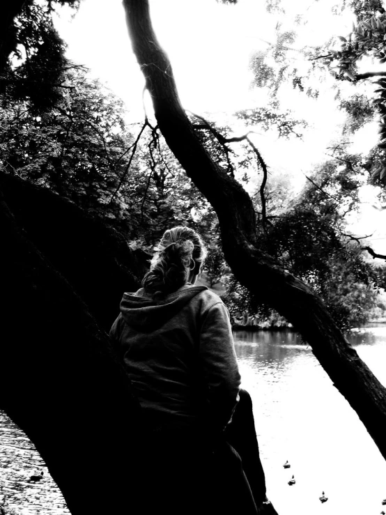 black and white pograph of person sitting on tree by the river