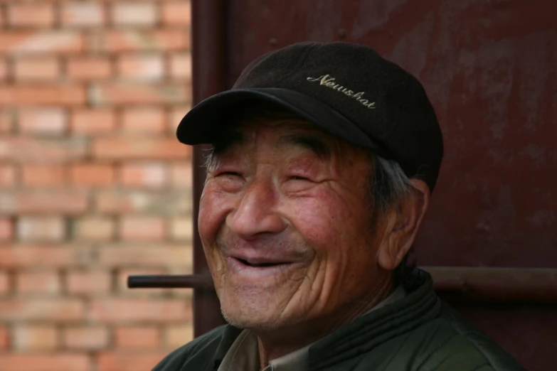 an older asian man wearing a black baseball cap and smiling at the camera