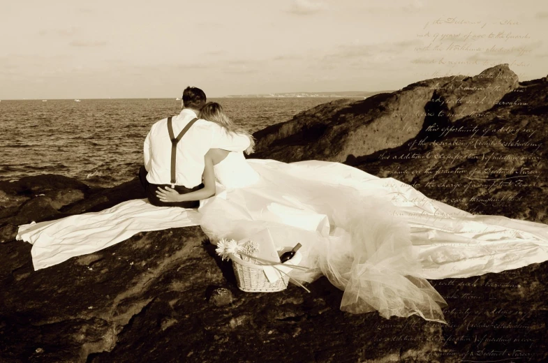 a man and woman sitting on rocks near the water