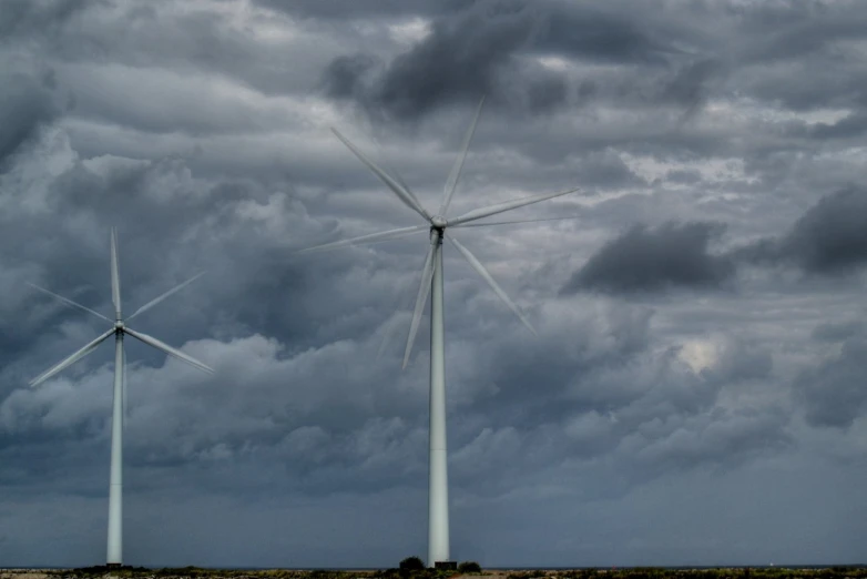 three windmills sitting in a field with dark clouds overhead