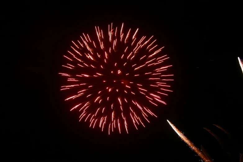 a red firework in the night sky with lots of small white fireworks