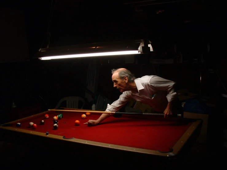 a man leans over while playing pool in the dark