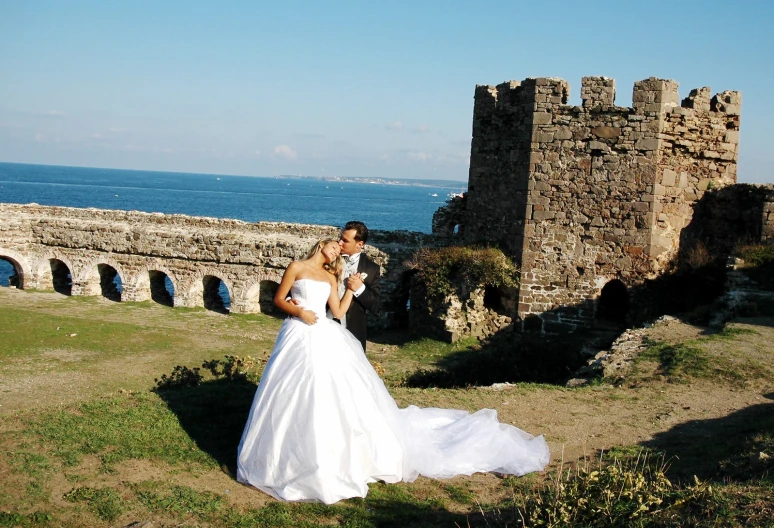 a bride and groom looking at each other while standing near a cliff