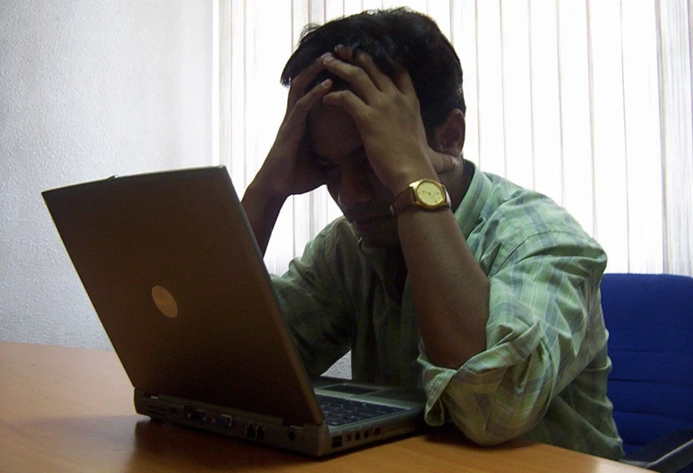 a man with his head in his hands looking at his laptop