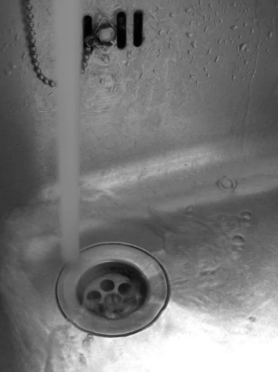 a chrome sink with no faucet, with the water flowing