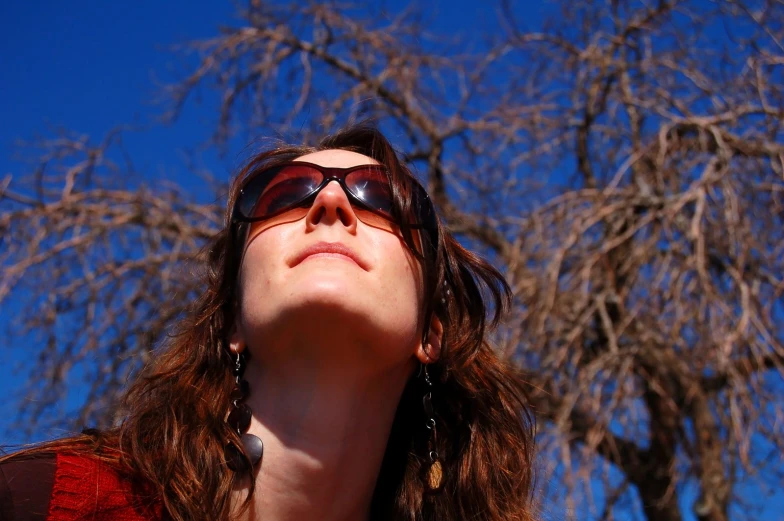a woman with sunglasses on standing in front of tree
