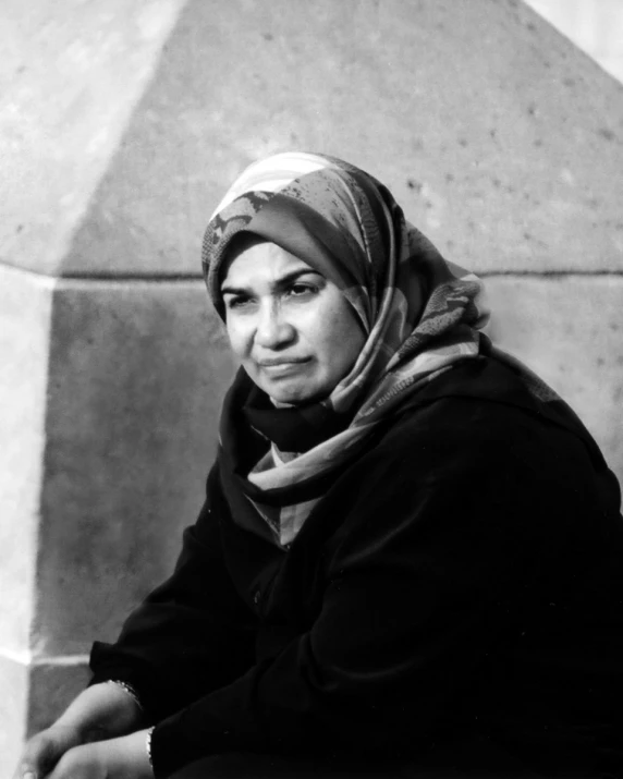 an old woman with a scarf on her head is sitting against a wall