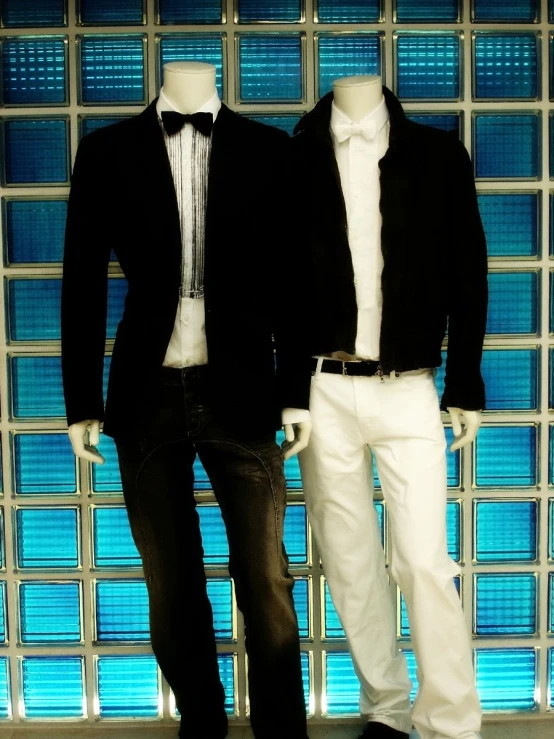 two white and black mannequins in front of a glass block wall