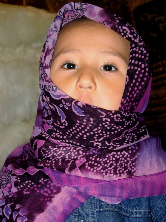 a young child wearing a purple scarf and looking into the camera