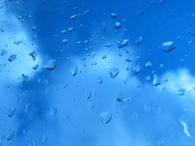 drops of water on a windshield with blue sky and clouds behind