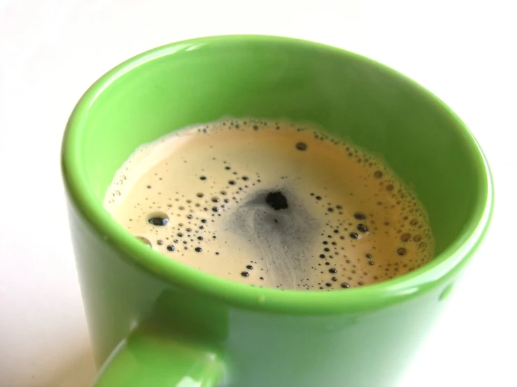 a green coffee cup filled with liquid on top of a white counter