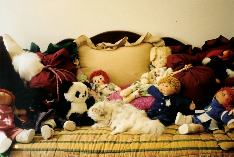 several toys including dolls and a cat are on a bed