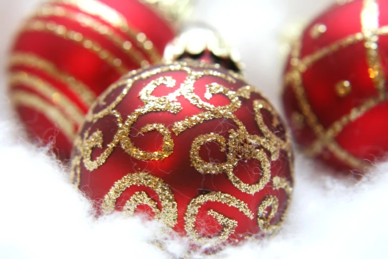 red ornaments covered with golden glitter sitting on a white surface