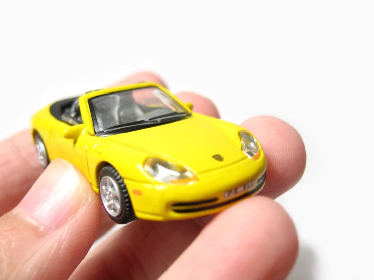 a hand holding a small yellow toy car