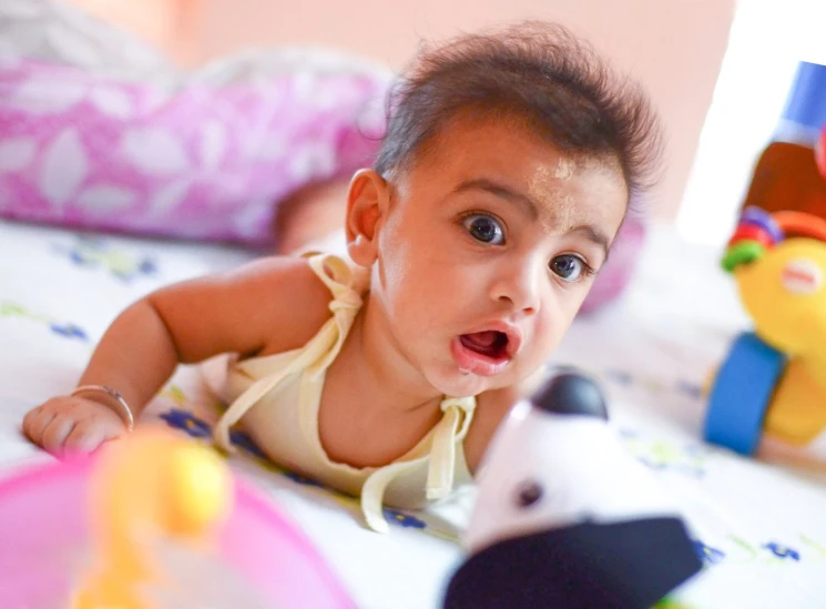 a very small baby laying on a bed with toys