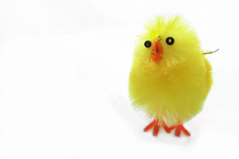 a yellow fuzzy chicken with black eyes, standing in the snow