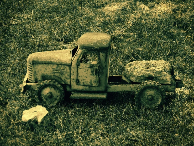 old toy truck with rock in its back sitting on grass