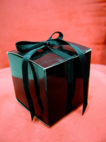 a black wrapped gift box with a bow on a pink surface