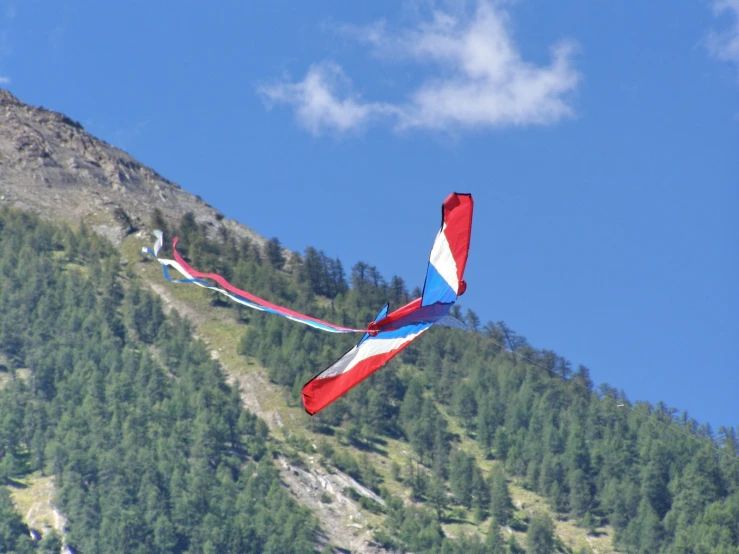 the large red, white and blue kite is flying in front of a mountain