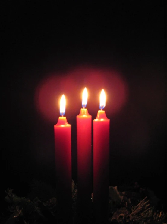 three lit candles with a dark background