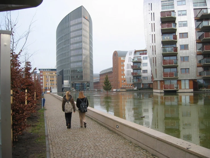 two women walking down a sidewalk on the side walk of a canal