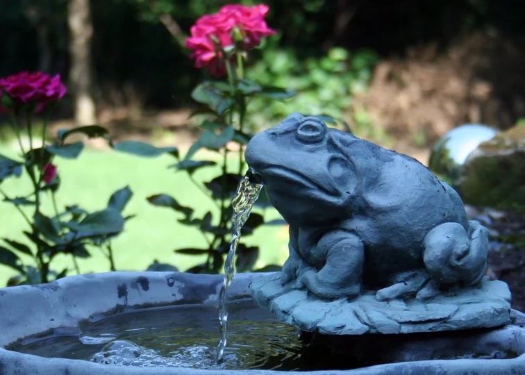 a water fountain with water pouring from it and flowers behind