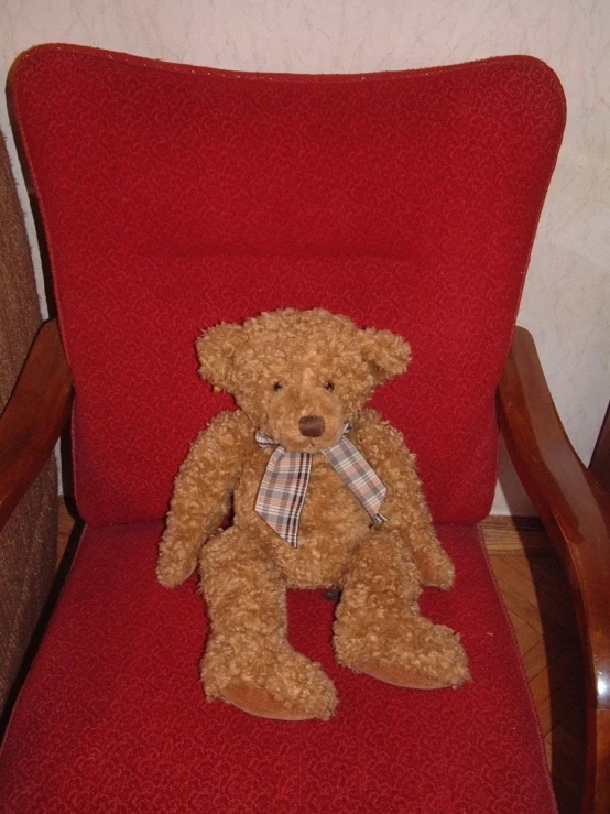 a brown teddy bear sits in a red chair